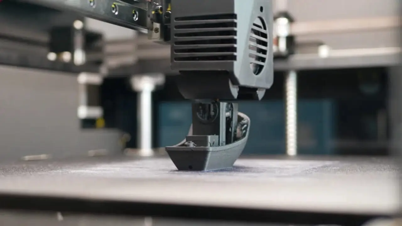 FDM 3D printer creating a plastic boat model layer by layer using filament extrusion technology.