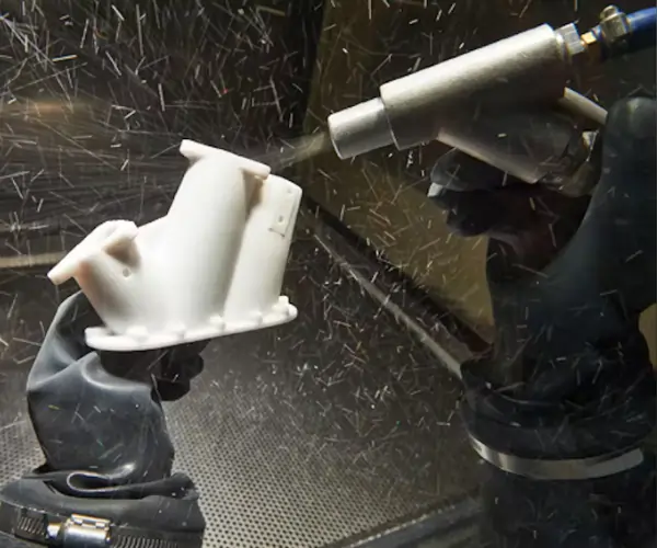 Operator using bead blasting to smooth MJF printed part surface for improved texture and finish.