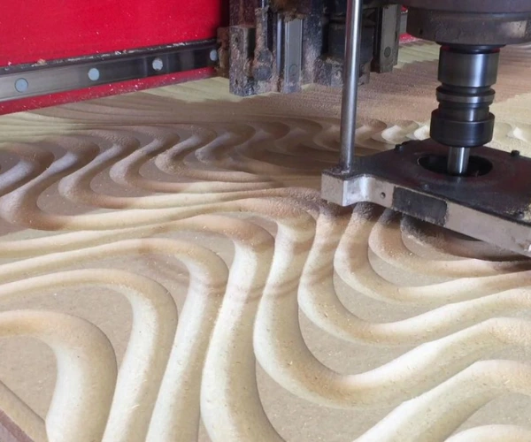 CNC machine carving a textured wavy pattern into wood.